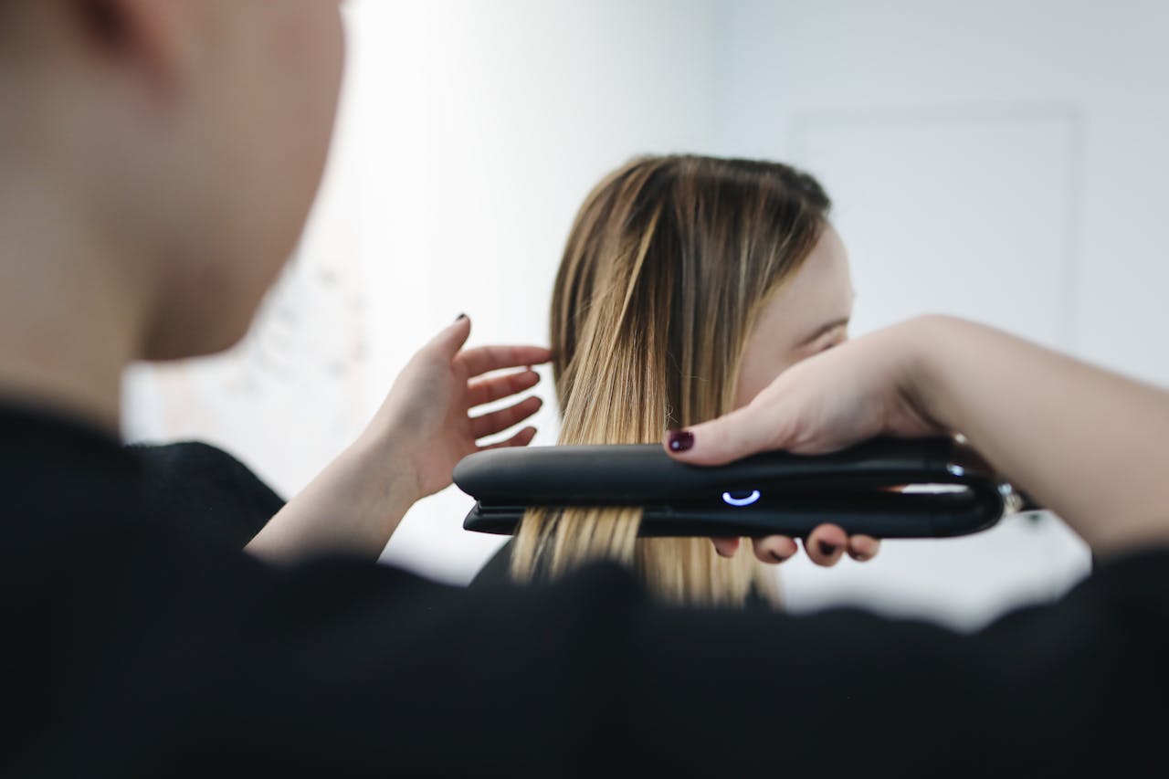 menu-02 Close-up of a hairstylist using a straightening iron for sleek hairstyle indoors.