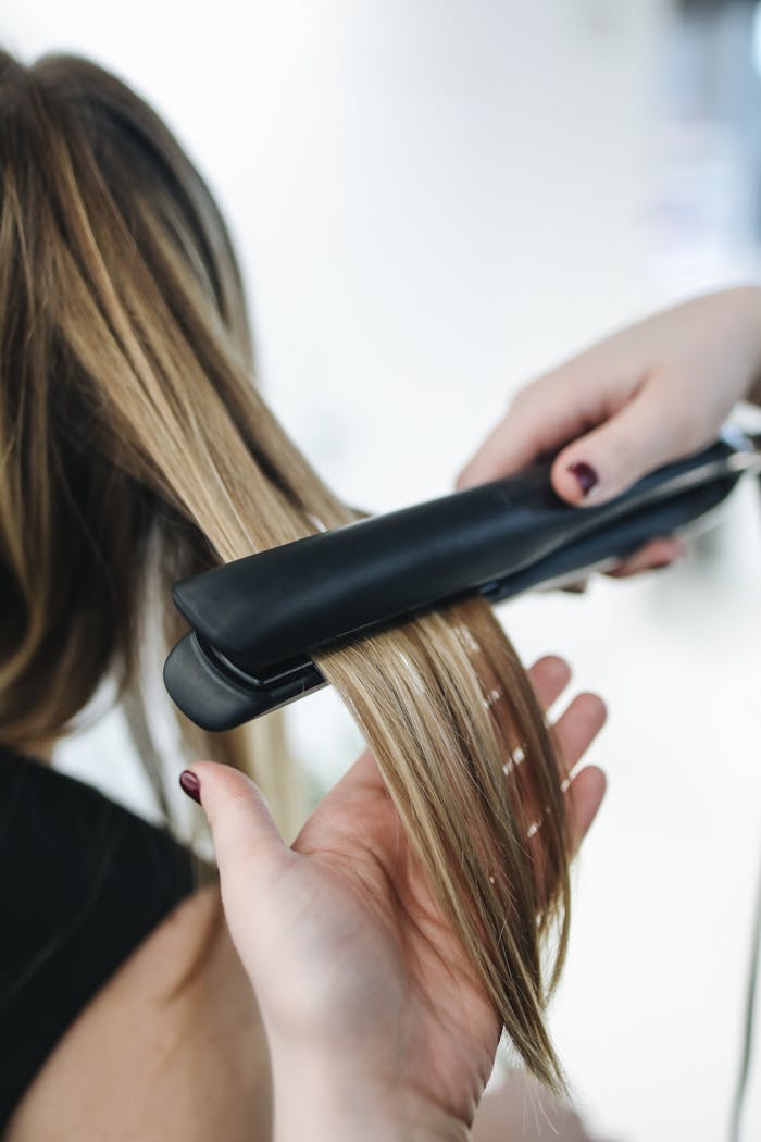 about-02 Close-up of a hairstylist using a flat iron on blonde hair in a salon setting.